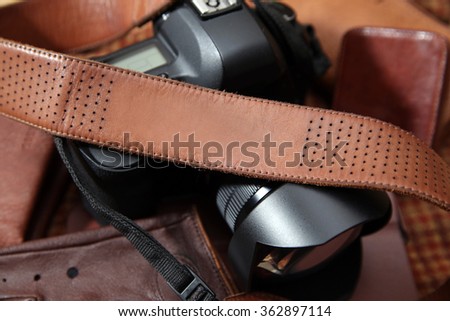 Photo camera with brown leather shoulder belt in brown background with leather accessories