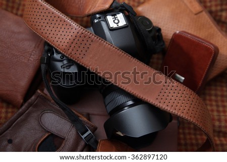 Photo camera with brown leather shoulder belt in brown background with leather accessories