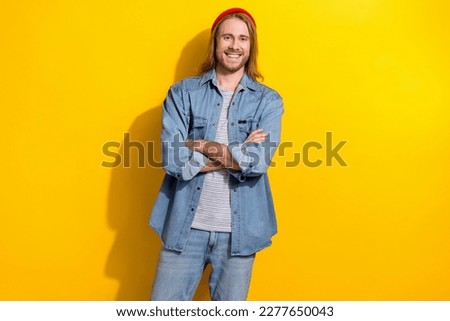 Photo of candid sincere guy with long hairstyle dressed jeans shirt holding arms folded smiling isolated on yellow color background