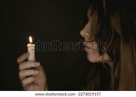 Photo of a candle at night holding by a young girl. Focus on the candle. Dark background. Scary horror concept