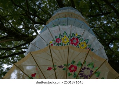 A photo captures a multi-colored umbrella hanging from a tree. The vivid colors shine against the soft, golden light filtering through the leaves, creating a magical and serene scene. - Powered by Shutterstock