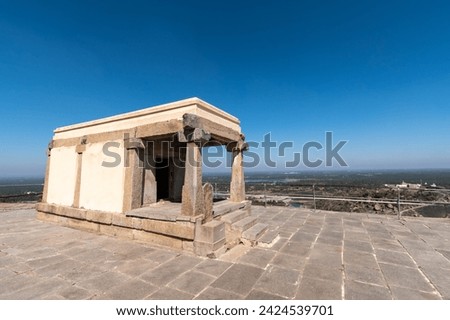 The photo captures a solitary stone temple structure on the summit of Shravanabelagola, featuring clear skies and a wide horizon in the backdrop.