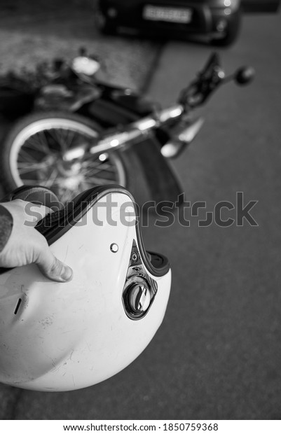 Photo\
of car, helmet in the hand of a man and motorcycle on road, the\
concept of road accidents, black and white\
photo.
