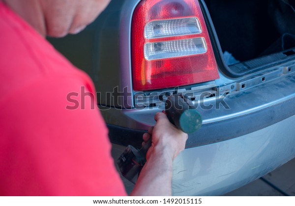 Photo of car\
mechanic fixing back of the car with automatic screwdriver.\
Transportation problems, car repair\
concept