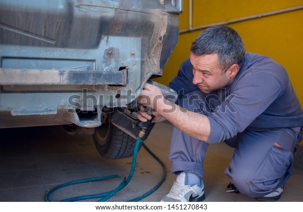 Photo of  car mechanics fixing  back of the\
car with automatic\
screwdriver.