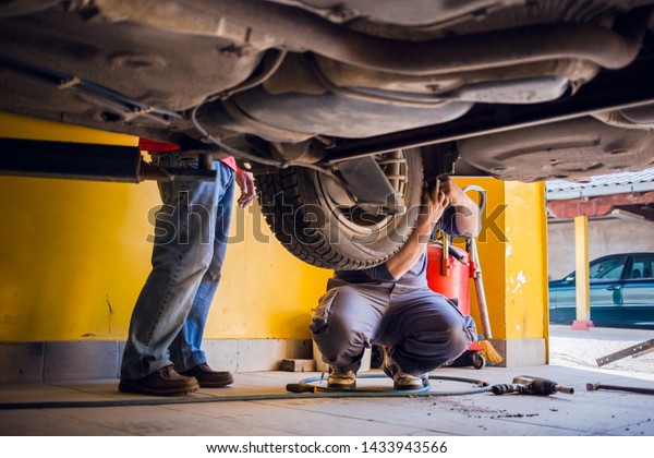 Photo of  car mechanics fixing the car. View from\
under the car