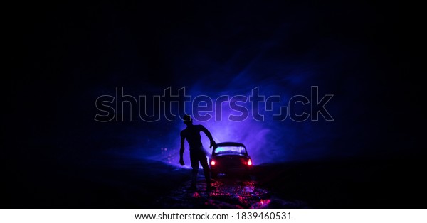 photo of a car stopped on the road lighting up a\
zombies. Silhouette terrible zombie night near the car. Miniature\
decoration. Selective\
focus