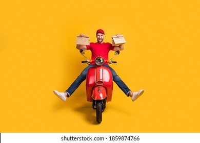 Photo of careless crazy guy drive bike hold two packages wear red t-shirt cap jeans isolated yellow color background