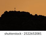 Photo of Catholic Cross on top of the rocky moutain at sunset. 