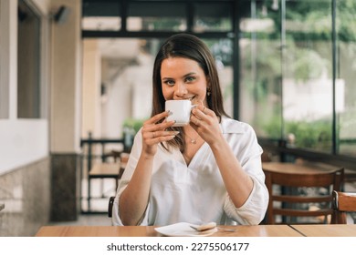 Photo of a Caucasian woman holding a cup of coffee. Concept of a person drinking coffee. Beautiful young woman sitting in a coffee shop - Powered by Shutterstock