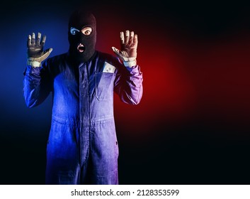 Photo of caught robber in mask, overalls, gloves and money pack standing on red and blue background.