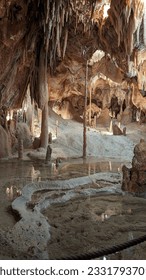 A photo of a cave chamber with naturally formed stalagmites, stalactites, columns and an underground lake.  