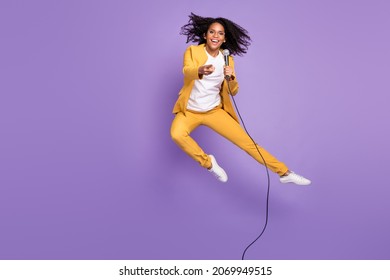 Photo Of Charming Confident Woman Dressed Yellow Suit Spectacles Holding Mic Jumping Isolated Violet Color Background