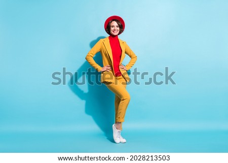 Photo of charming confident young lady wear yellow blazer red cap smiling arms waist isolated blue color background