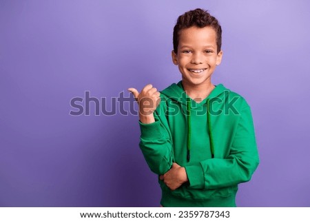 Photo of charming cool small boy wear green sweatshirt showing thumb empty space isolated violet color background