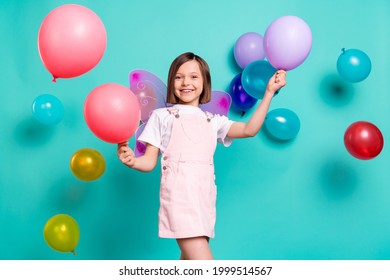 Photo of charming funny school girl wear pink overall wings smiling playing balloons isolated teal color background