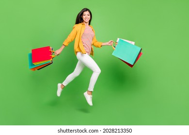 Photo of charming funny young lady wear yellow shirt smiling holding bargains walking jumping isolated green color background