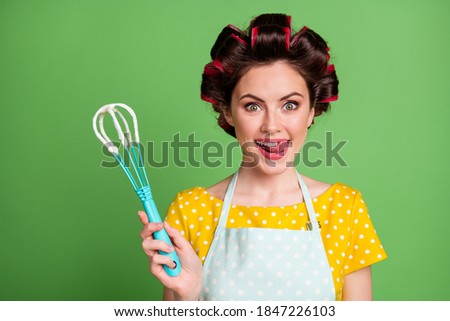 Photo of charming girl lady roller hairdo stick out tongue lick teeth hold whisk try meal shocking yummy taste addicted hobby cooking wear dotted apron shirt isolated green color background