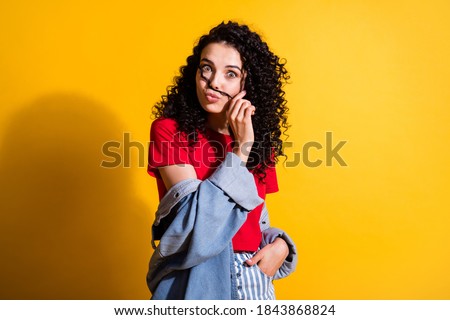 Photo of charming girl play curl hold mustachio pout lips wear red top striped jeans jacket isolated yellow color background