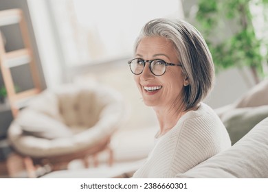Photo of charming good mood elderly lady wear white cardigan spectacles smiling indoors apartment room