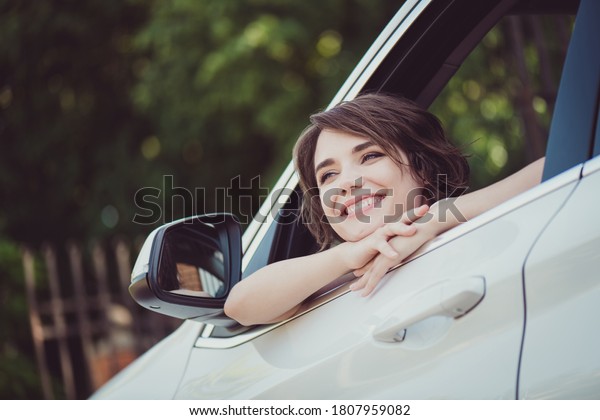 Photo of\
charming lovely lady smiling face hands chin dreamy cheerful look\
out of car window rearview mirror handle watching birds singing\
cherry blossom wear white shirt\
indoors