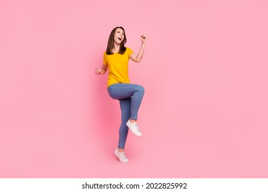 Photo of charming lucky young woman dressed yellow t-shirt rising fists looking empty space isolated pink color background