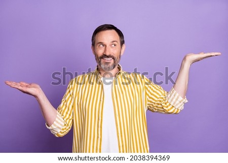 Photo of charming mature happy man look hold hands empty space compare scales isolated on purple color background