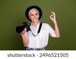 Photo of charming positive camerawoman wear white shirt hat showing okey sign tacking photo isolated green color background