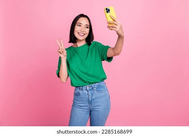 Photo of charming positive lady hold smart phone make selfie demonstrate v-sign isolated on pink color background