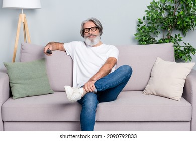 Photo Of Charming Positive Man Pensioner Dressed White T-shirt Spectacles Having Rest Sofa Watching Tv Indoors Isolated Grey Color Background