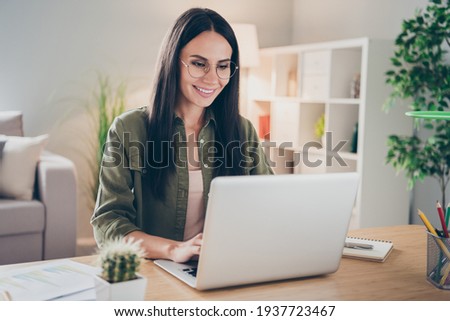 Photo of charming positive person sit behind desktop look use laptop have good mood working home indoors