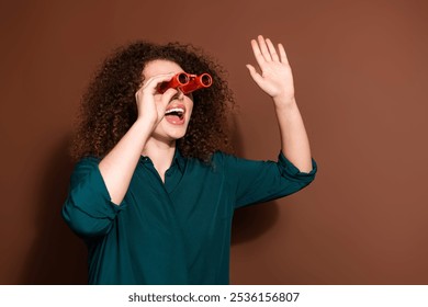 Photo of charming positive woman wear green shirt looking binoculars waving hello empty space isolated brown color background - Powered by Shutterstock