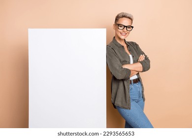 Photo of charming pretty lady dressed khaki shirt arms crossed white placard emtpy space isolated beige color background