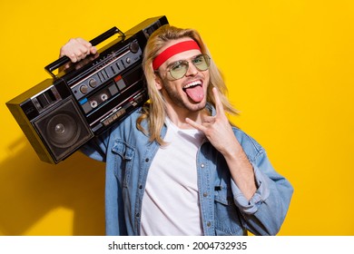 Photo Of Charming Rude Guy Dressed Denim Shirt Smiling Showing Tongue Rock Sign Holding Boom Box Isolated Yellow Color Background