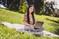 Photo Of Charming Shiny Young Lady Wear Checkered Shirt Smiling Sitting Grass Chatting Modern Device Outdoors Urban City Park