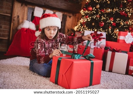 Photo of charming shocked school girl wear print pullover headwear sitting floor opening huge present indoors house home room