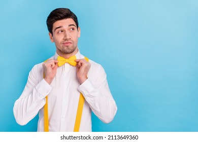 Photo of charming thoughtful guy dressed white shirt correcting yellow bowtie looking empty space isolated blue color background