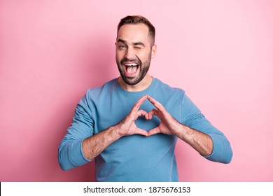 Photo of charming young guy wear blue pullover winking showing heart fingers isolated pink color background