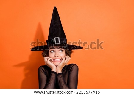 Photo of charming young lady look empty space frighened bite nails wear stylish black halloween witch clothes isolated on orange background