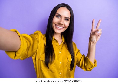 Photo of cheerful adorable lady blogger make selfie hand demonstrate v-sign greeting symbol isolated on purple color background