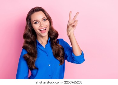 Photo of cheerful adorable lady wear blue clothes arm demonstrate v-sign good mood empty space isolated on pink color background