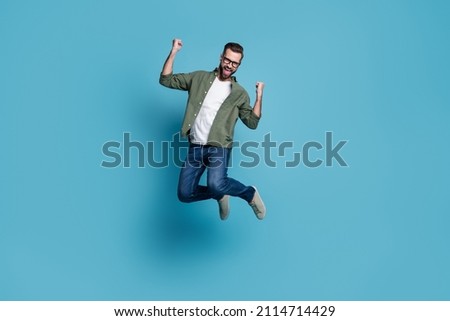 Photo of cheerful astonished guy jump rejoice triumph wear specs green shirt isolated blue color background