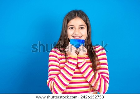 Photo of cheerful beautiful kid girl wearing striped t-shirt hold debit card look empty space