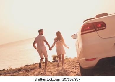 Photo of cheerful carefree married couple dressed white clothes driving car walking beach holding arms outdoors country side road