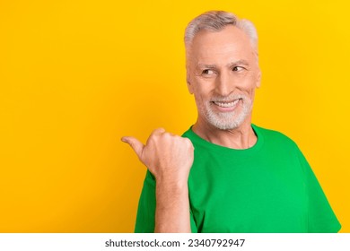 Photo of cheerful cool man wear green t-shirt looking showing thumb back empty space isolated yellow color background