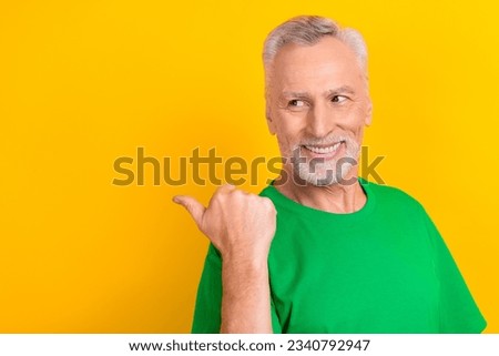 Photo of cheerful cool man wear green t-shirt looking showing thumb back empty space isolated yellow color background