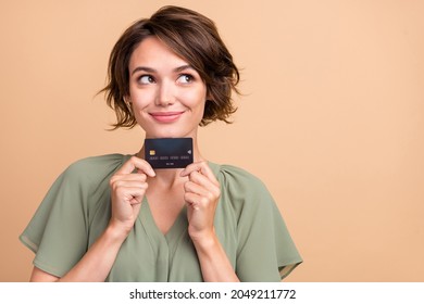 Photo of cheerful dreamy girlish lady hold debit card look empty space wear green dress isolated beige color background