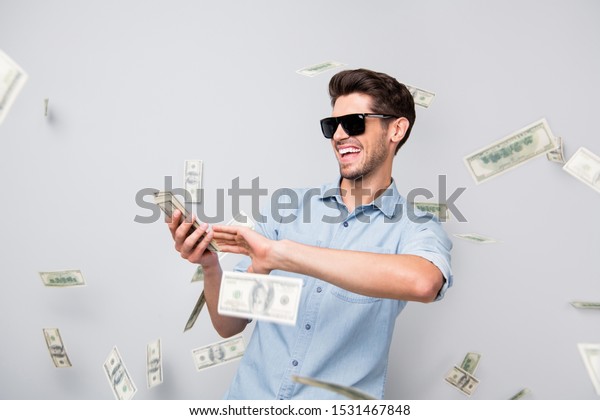 Photo of cheerful excited ecstatic overjoyed\
man throwing money away showing his wealthiness wearing denim\
isolated over grey color\
background