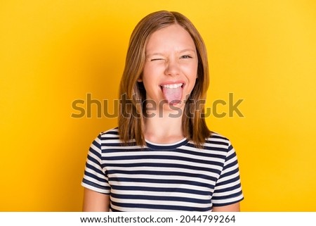 Photo of cheerful excited little girl eye wink tongue out have good mood look camera isolated on yellow color background