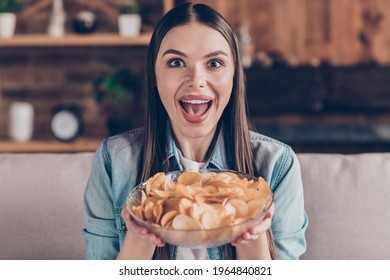 Photo of cheerful excited young woman hold hands plate snacks potato chips eat food indoors inside house